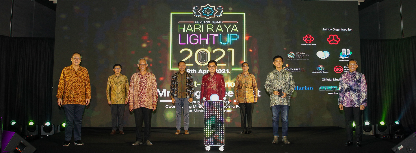 Group of people on a stage with "Hari Raya Light Up 2021" backdrop and logos.